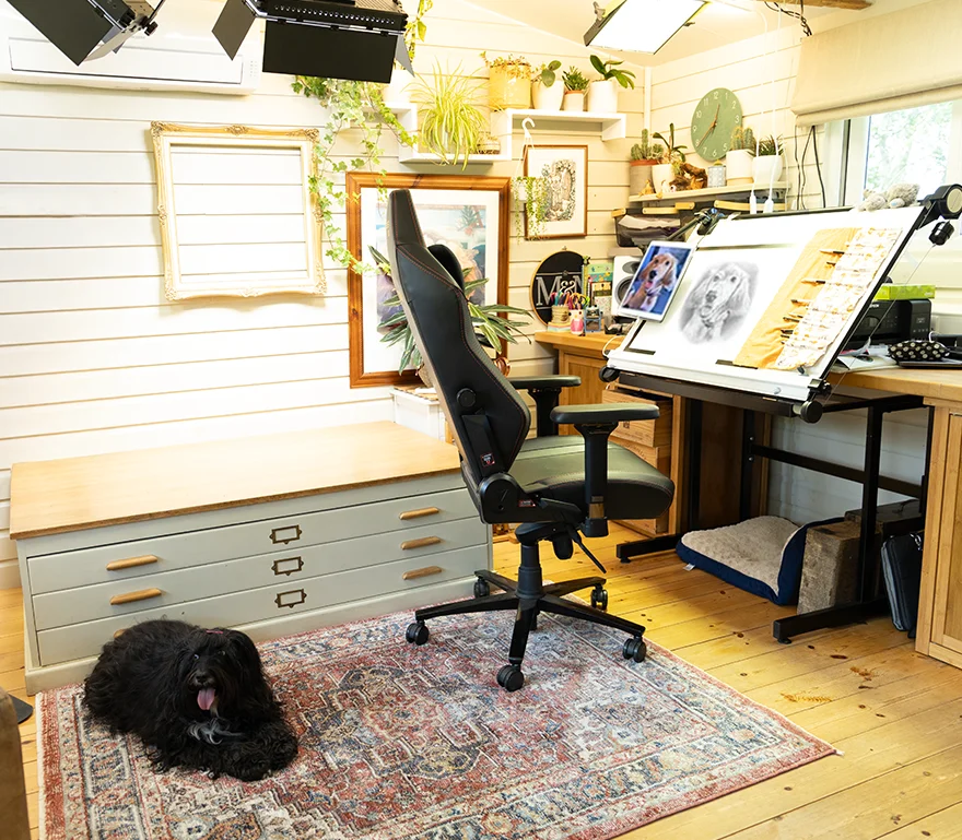 Melanie's Dedicated Studio Workspace for Pencil Drawings Melanie's organized drawing desk inside the art studio, featuring a tilted drawing board, laptop, and monitor setup for pencil portraits.